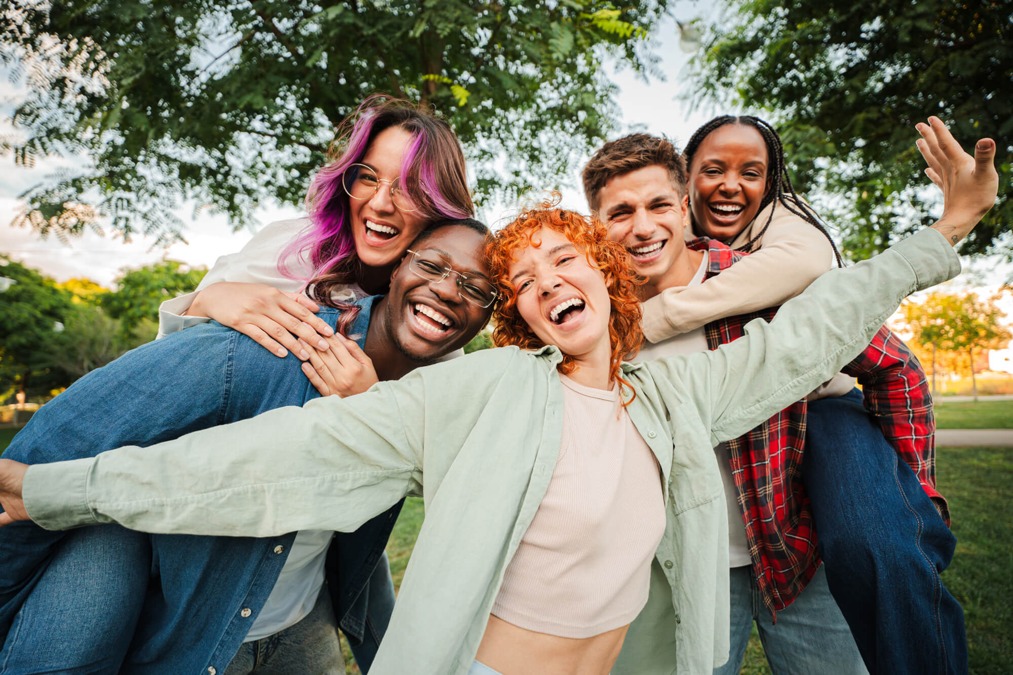 A diverse group of five young adults laughing and embracing outdoors in a park, representing community support in opioid overdose awareness