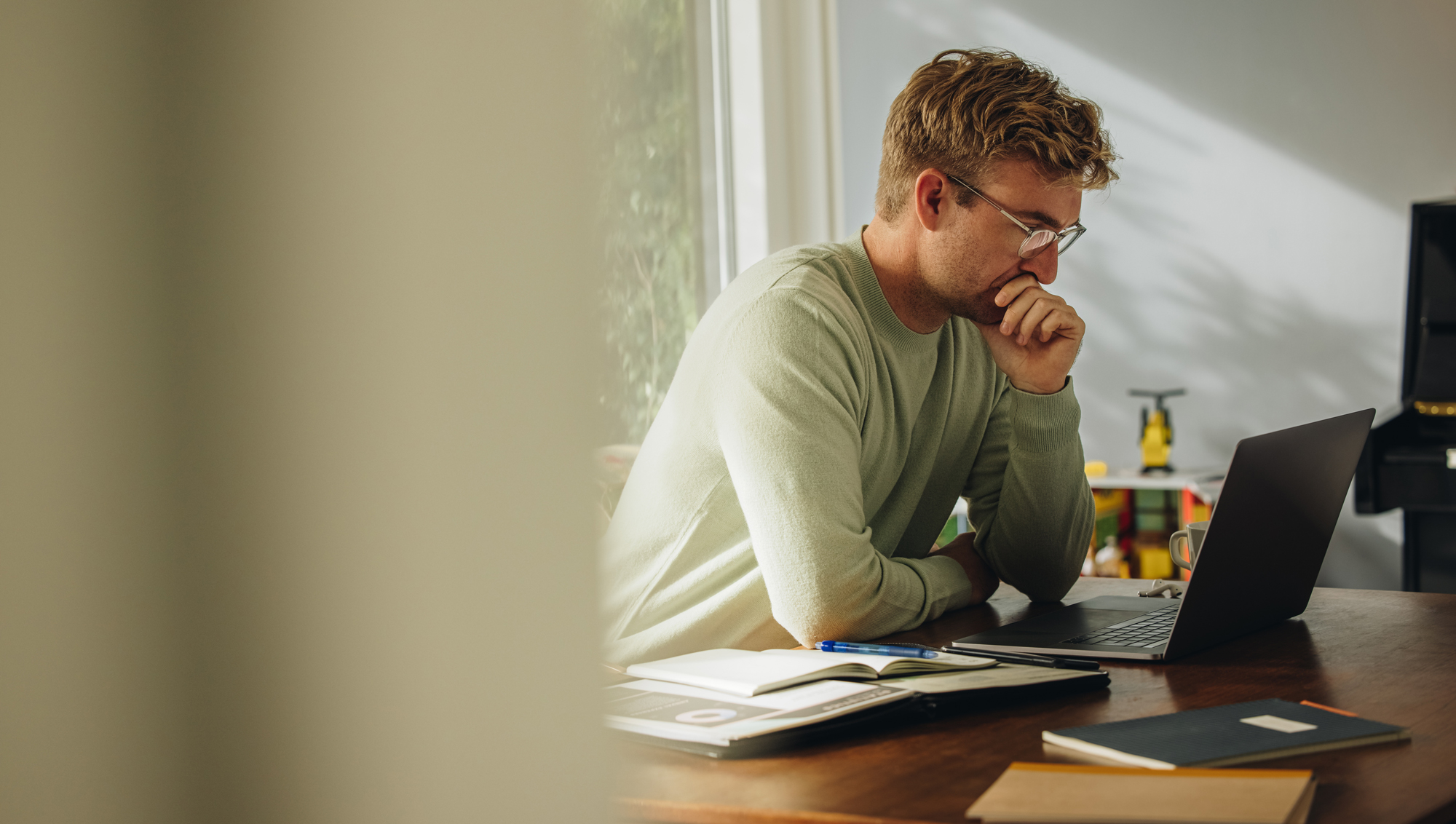 Man sitting at a desk, deep in thought while looking at his laptop, considering whether it's time to ask for help