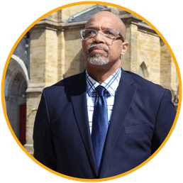 Keynote speaker Nathan Ivy, nonprofit executive director, wearing a navy suit and glasses, photographed outdoors.
