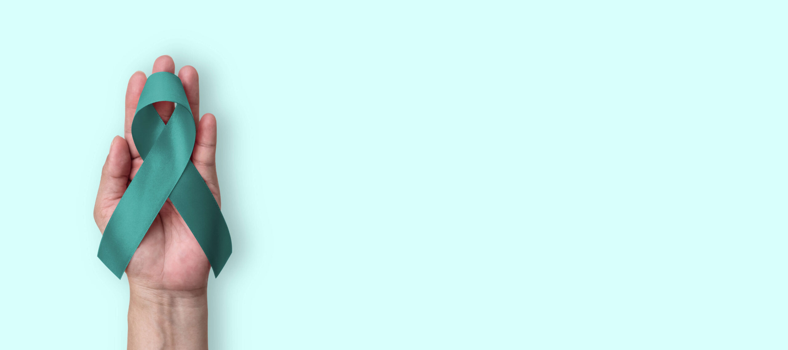 ptsd-awareness-month-teal-ribbon-gibson-center.jpg-2 A hand holding a teal ribbon against a light blue background, representing PTSD Awareness Month